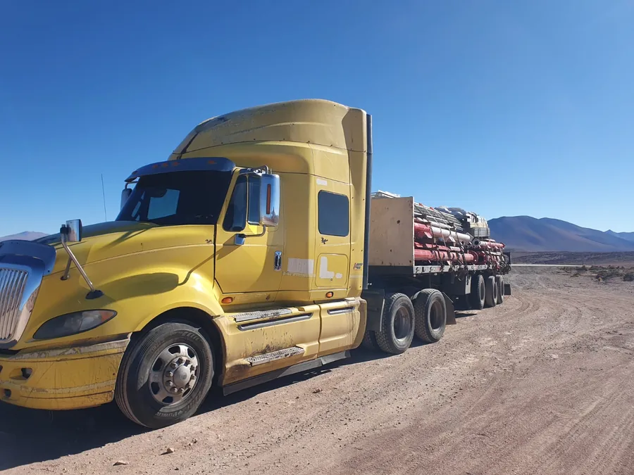 Tractocamión International amarillo con estructura amarrada sobre cama plana, con la cordillera de fondo