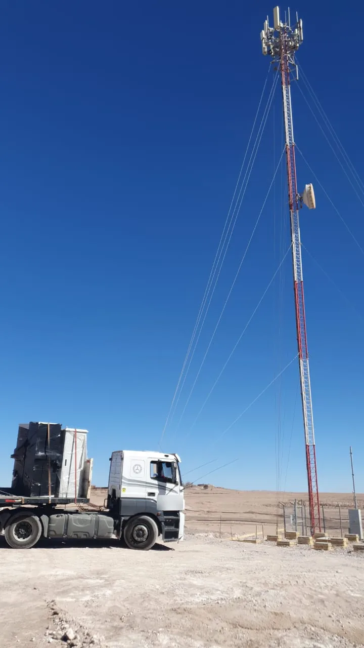 Torre de telecomunicaciones roja y blanca en faena del desierto, con un tractocamión cargado junto a su base